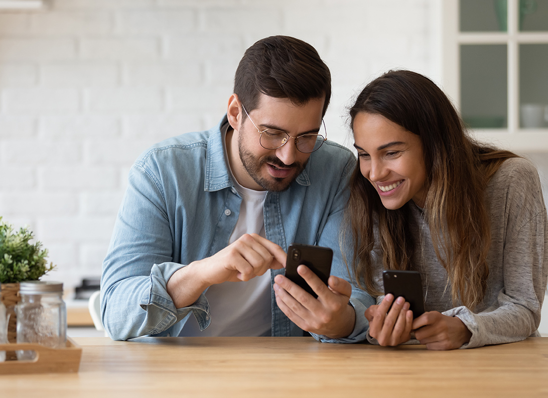 Read Our Reviews - Man Pointing to His Phone While Girl Smiles and Looks While Holding Her Phone and They are Standing at a Counter in a Modern Kitchen